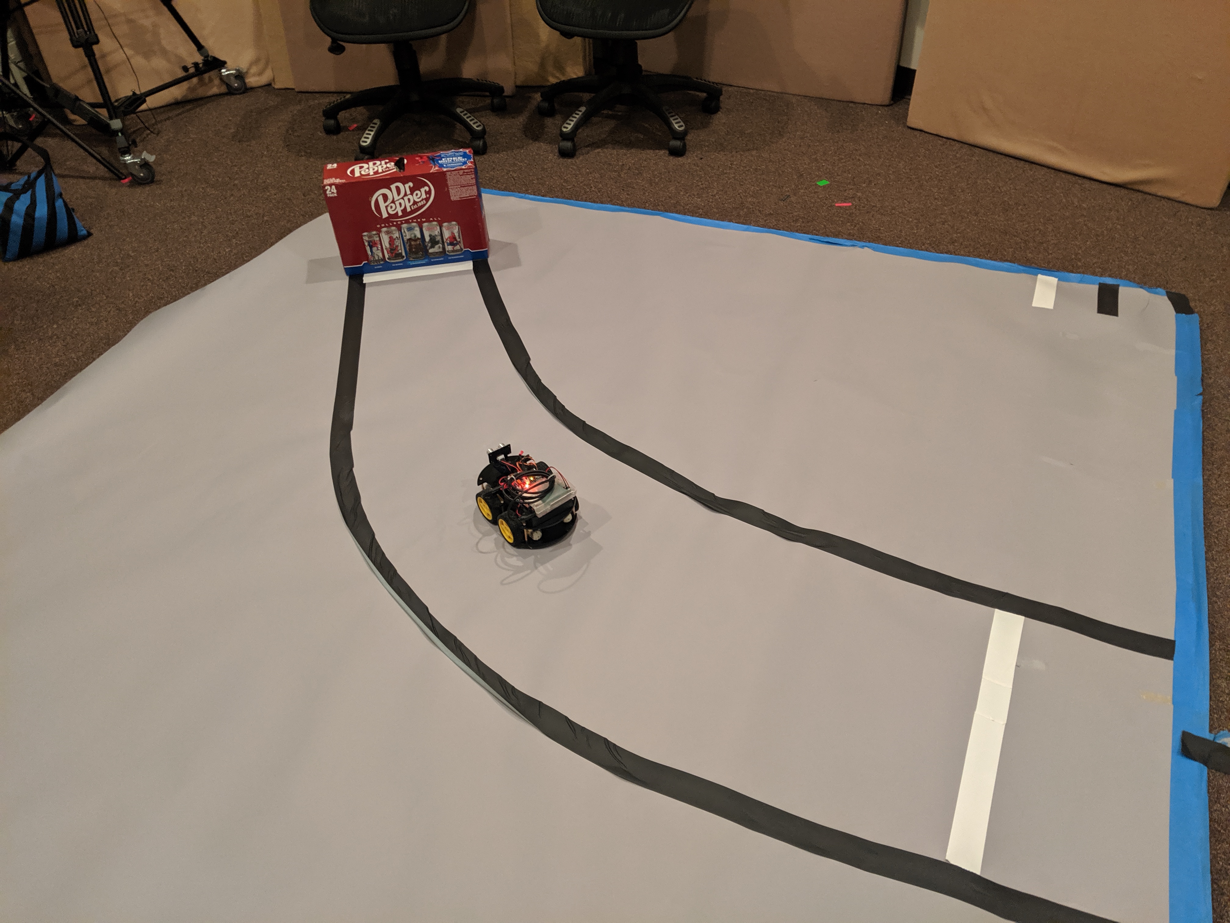 The robot car is centered between the black tape guides as it follows a curved path toward the finish line
