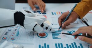 Several hands rest on a page of charts, collaborating on editing. 3 hands are human; one is a robot's.