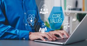 A blue-shirted worker's hands hover over a laptop. Large icons illustrating core values like balance and cooperation overlay the image.