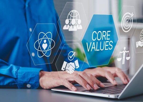 A blue-shirted worker's hands hover over a laptop. Large icons illustrating core values like balance and cooperation overlay the image.