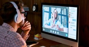 A man wearing headphones intently watches a video showing a woman presenting