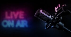 A blue and pink neon sign reads 'Live On Air' against a black background with a large dark gray and silver mic in the foreground