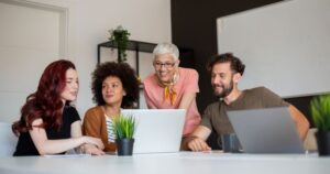 People of different ages cluster around a computer screen. All are smiling.